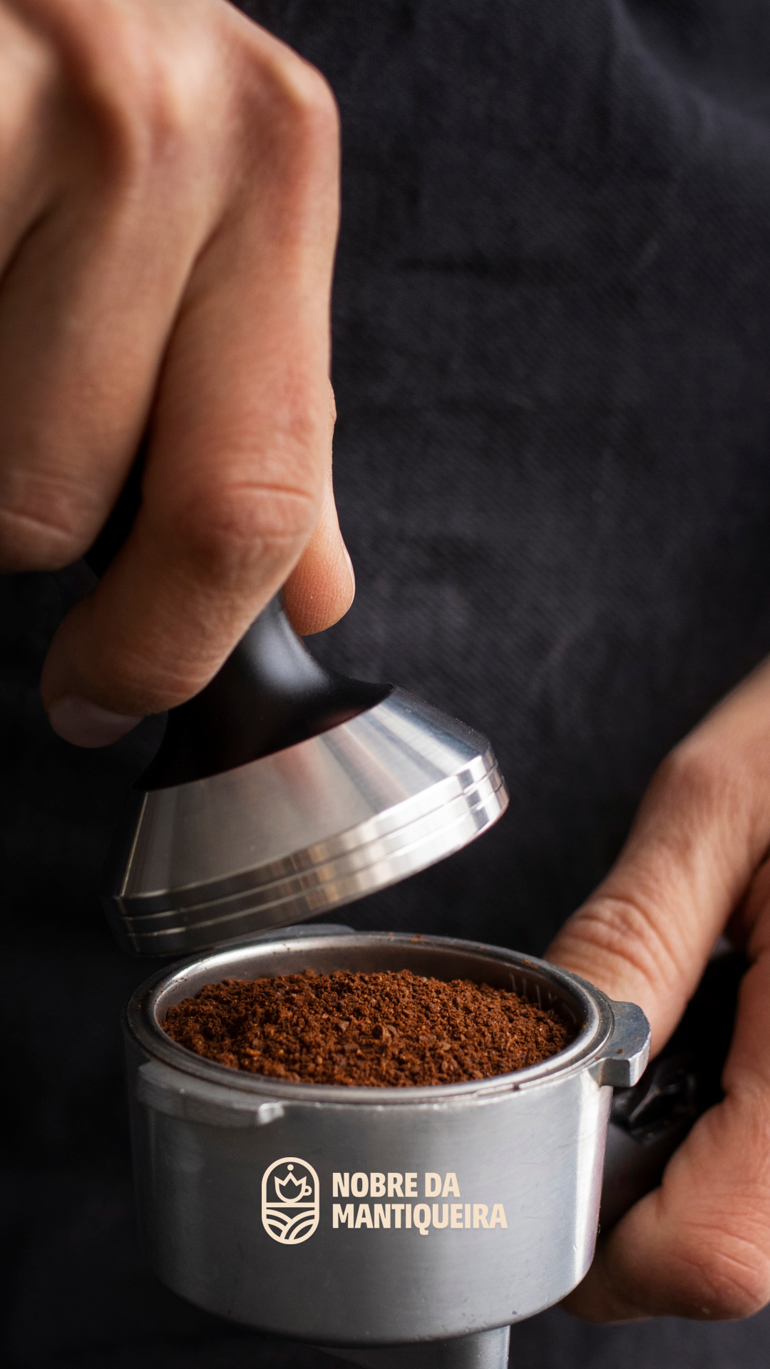Mãos preparando café com tamper sobre porta-filtro, com logomarca Nobre da Mantiqueira